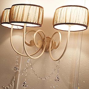 AVRIL L.50 H.30 P.26 cm</br> 
_Applique Avril in metallo lavorato con 3 luci, finitura perla, cat. C, e paralumi plissè in tessuto e pendenti Swarovski Crystal