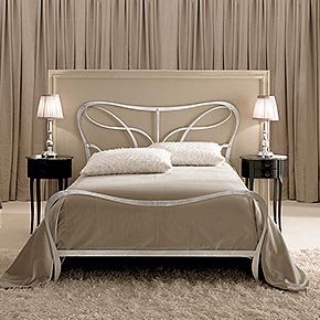 _Letto in lamiera massiccia tagliata al laser e lavorata a mano finitura foglia argento, cat. C</br>
_Copriletto a fazzoletto in tessuto Velvet/57, cat. B</br>
_Comodini Ovalino in legno con maniglia Ricciolo in metallo, finitura ebano antico, cat. B</br>
_Abatjour Rina in legno, finitura foglia argento, cat. C, con paralume Plissé in tessuto Thea/35, cat. A</br>
_Poltrona Regina capitonnè</br>
_Armadio Liberty 2 ante in legno, finitura Canova grigio, decoro Aurora